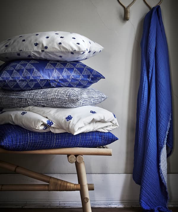 Blue and white patterned cushions piled up on a rattan bench and blue fabric hanging from a hook.