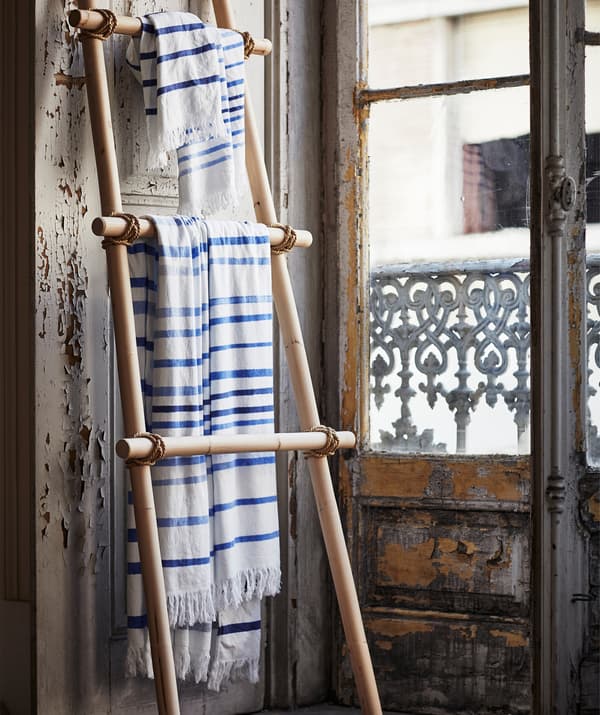 Blue and white striped fabric hanging on a wooden ladder shelf leaning against a wall.