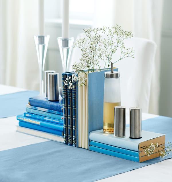 Blue books are arranged with candles, baby’s breath flowers, salt and pepper shakers, and oil to create a centrepiece.