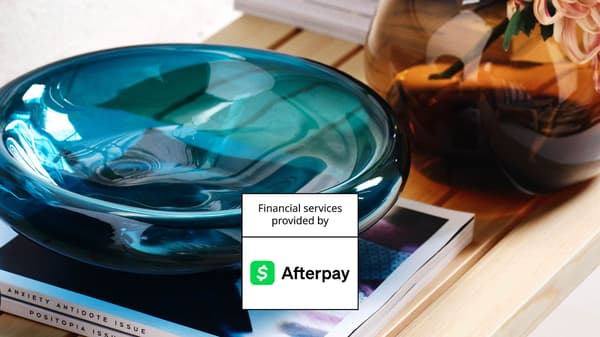 Blue glass decor bowl on books beside a vase, with Afterpay financing badge overlay.