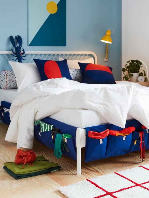 Blue MÖJLIGHET textile bed pockets used as storage for socks, suspenders and more, hung on the sides of a bed.