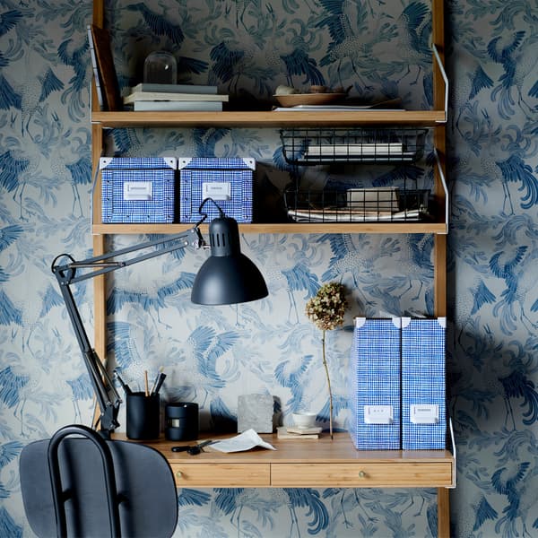 Blue patterned boxes and files on a wooden desk with built-in shelves and a black work lamp.