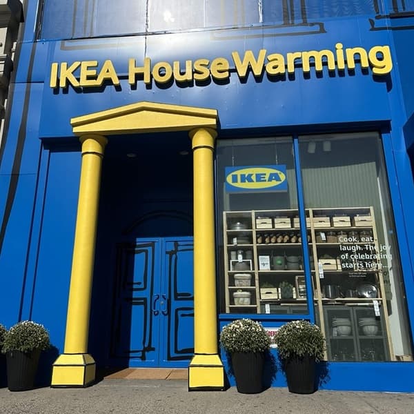Blue storefront with yellow columns and sign reading 'IKEA House Warming,' window displays kitchen items.