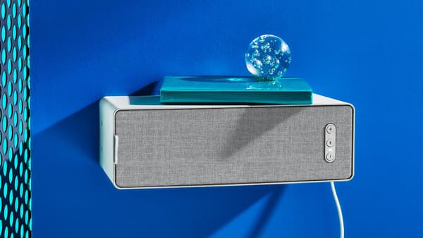 Bluetooth reproduktor připevněný na modré stěně, na kterém je položená modrá kniha a skleněná dekorační koule.