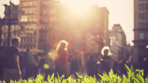 Blurred image of grass and people walking along a busy street
