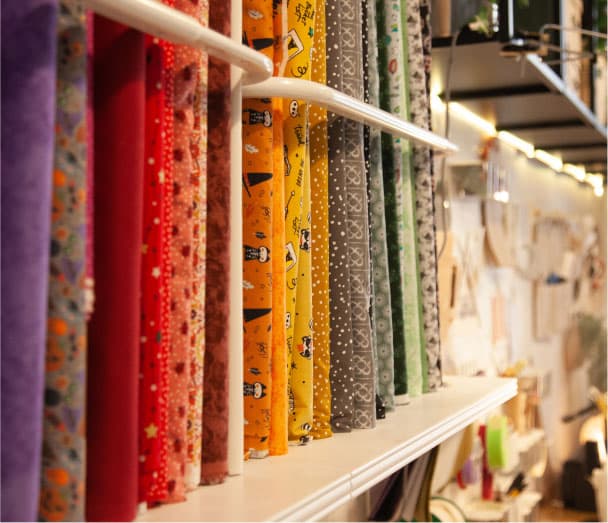 Bobines de teles de colors vius i estampats variats exposades en una prestatgeria d’un taller o botiga de costura.