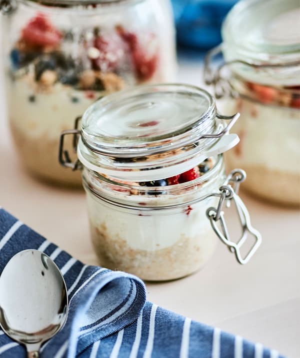 Bocaux de différentes tailles remplis de flocons d'avoine, de yaourt et de fruits près d'une serviette bleue et blanche et d'une cuillère.
