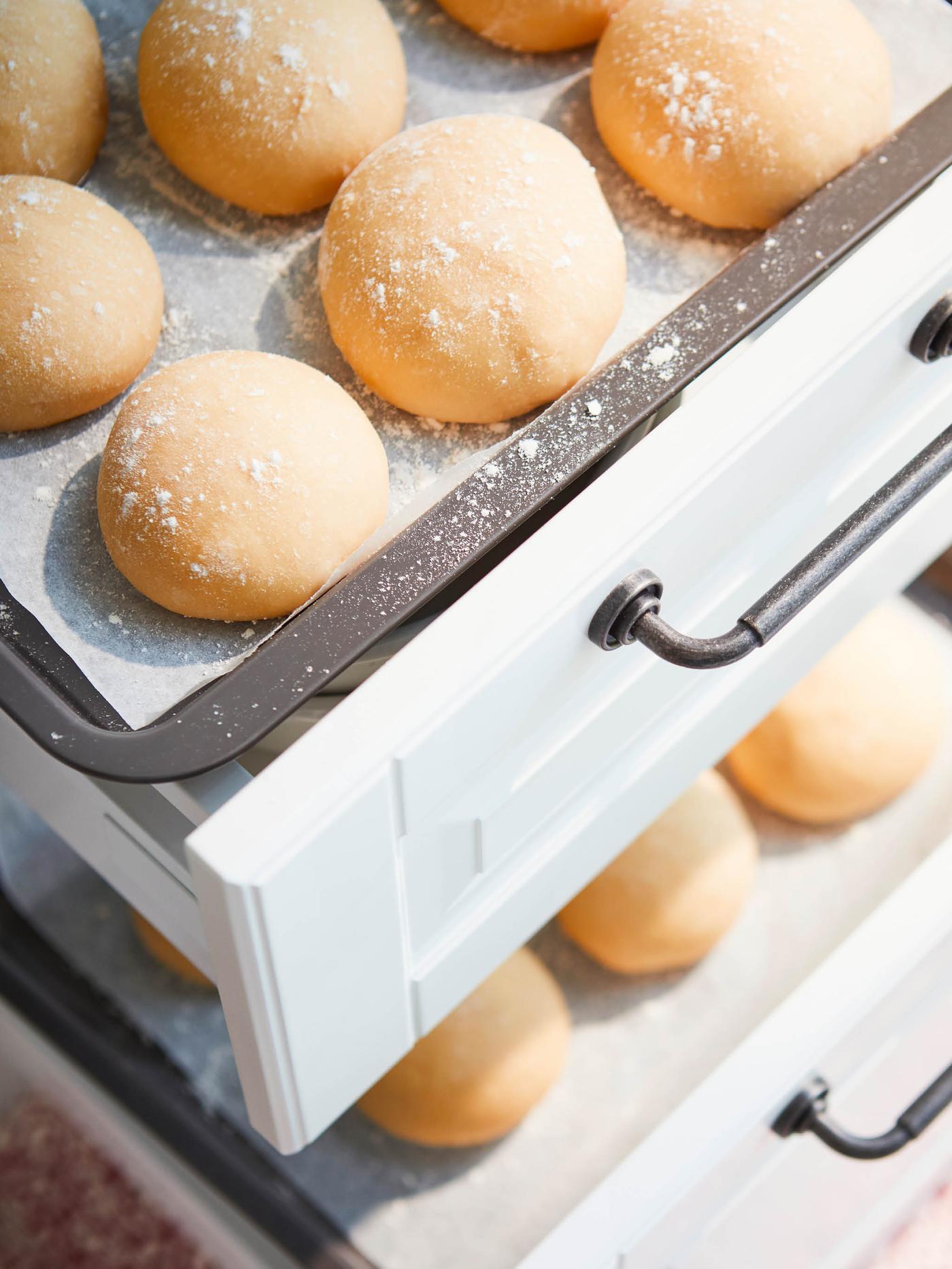 Bochánky těsta kynou na plechu na pečení HEMMABAK, který je položený na zásuvce kuchyňské skříňky.