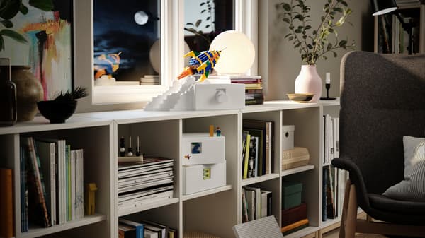 Boîte blanche sur un système de rangement KALLAX, à côté d’une fusée en briques LEGO.