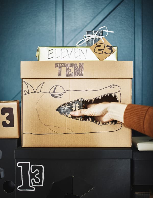 Boîte en carton avec un crocodile dessiné dessus et main plongeant à l'intérieur pour aller chercher le cadeau.