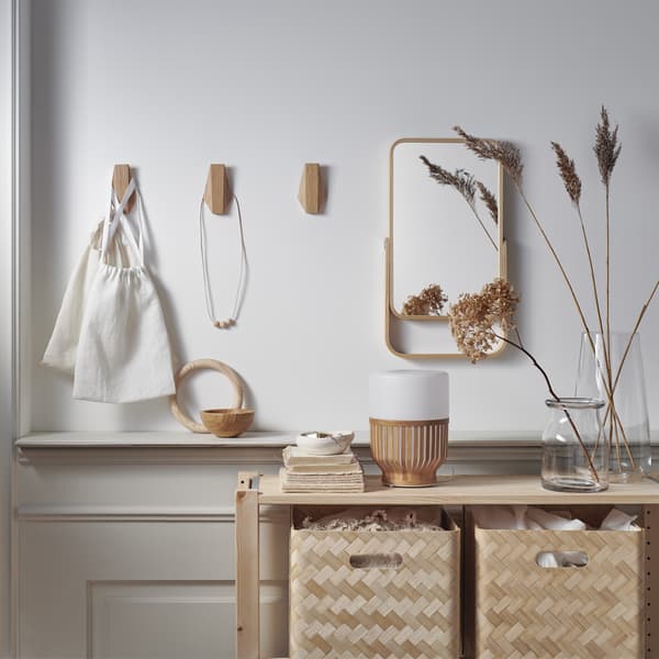 Boîtes de rangement en bambou sur une étagère en bois, un miroir et des crochets en bois sur un mur blanc.