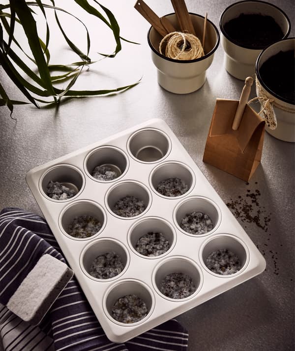 Bol mare din sticlă cu strecurătoare IDEALISK cu mare parte din pulpa de hârtie obținută din șervețelele rupte, lângă trei ghivece. 