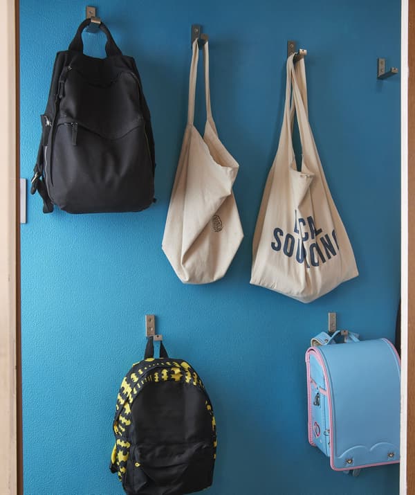 Bolsas e mochilas colgan de ganchos a diferentes alturas nunha parede azul.