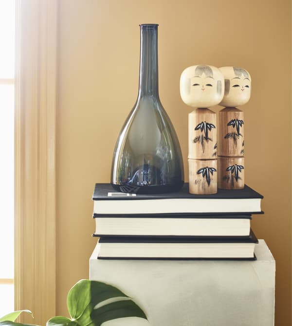 Books, a vase, and figurines sit on top of a pedestal.