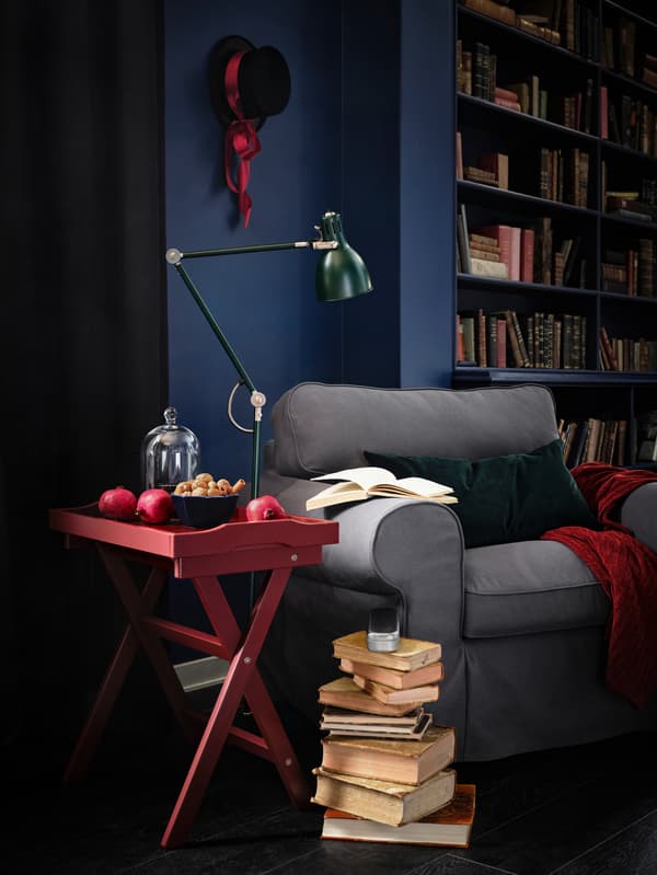 Books are piled up next to a cosy-looking EKTORP armchair with a red table and green lamp stood next to it.