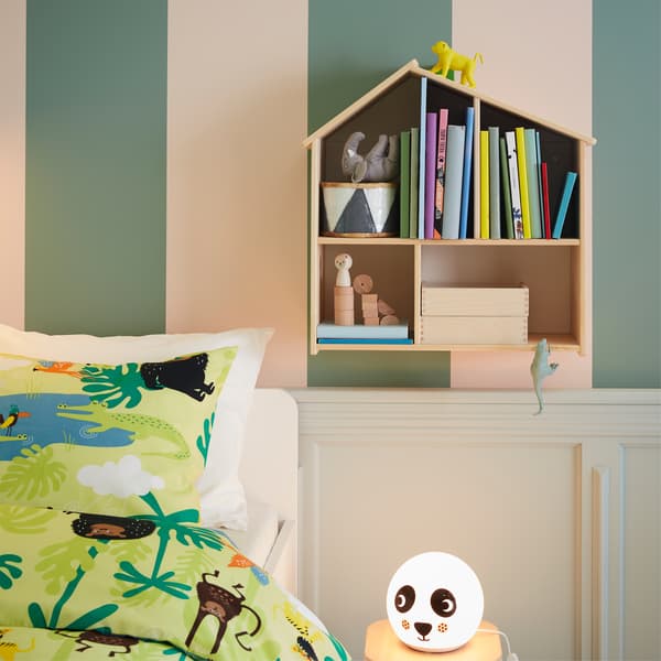 Books in a dollhouse mounted on a wall, jungle patterned bed textiles and a panda patterned table lamp.
