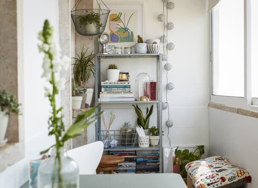 Books, plants and decorative items displayed on a tall, open shelving unit against a white wall.