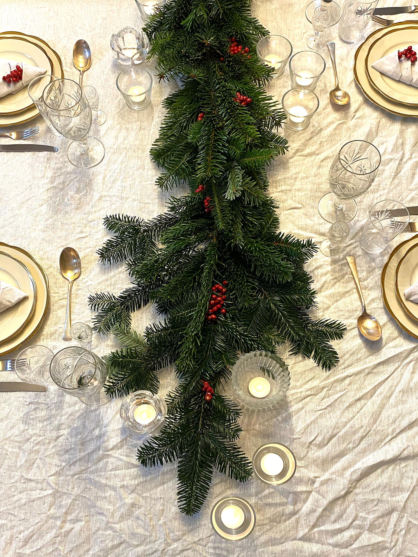 Borddekorasjon ovenfra. Vi ser girlander som ligger utover bordet med hint av rødt i seg, knyttet til jul