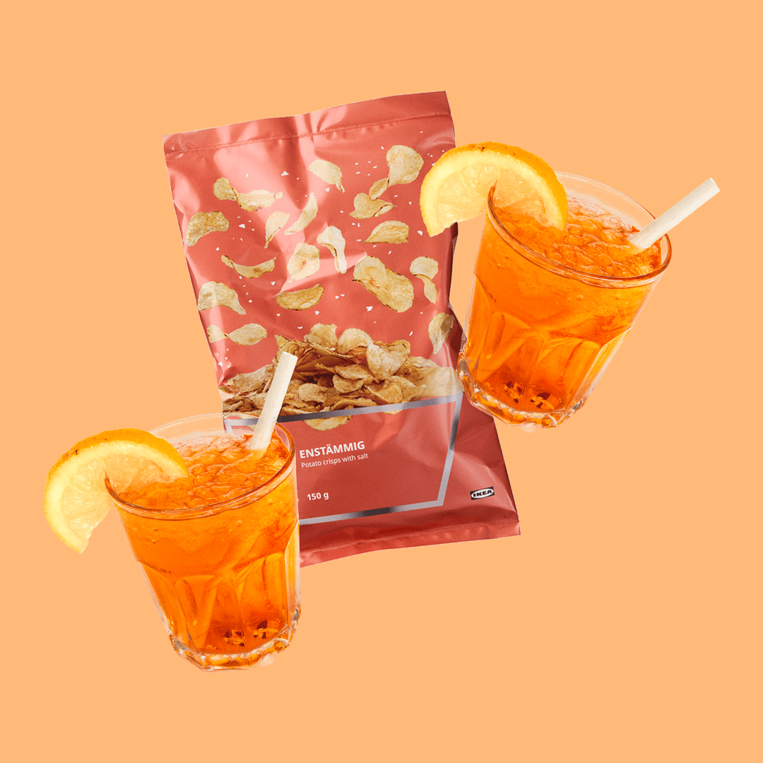 Bossa de patates fregides ENSTÄMMIG amb dues begudes Spritz de taronja amb gel i rodanxes de taronja, sobre un fons taronja.