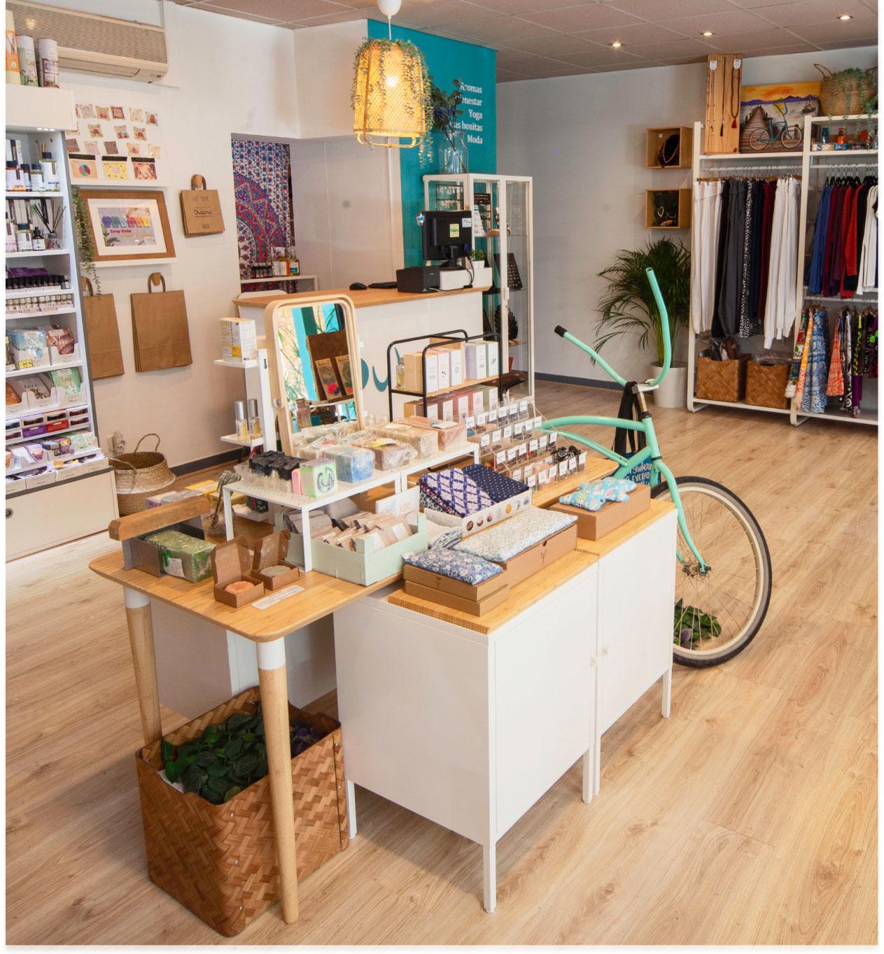 Botiga acollidora amb productes naturals, cosmètics, roba i una bicicleta decorativa al costat del taulell.