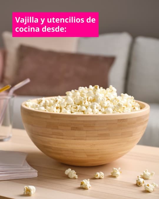 Bowl de madera con palomitas sobre una mesa clara en una sala de estar, junto a vasos y papeles. Texto en imagen dice: “Vajilla y utensilios de cocina desde:”.