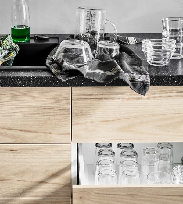 Bowls being dried on a worktop above an open, ash effect drawer filled neatly with rows of glass cups