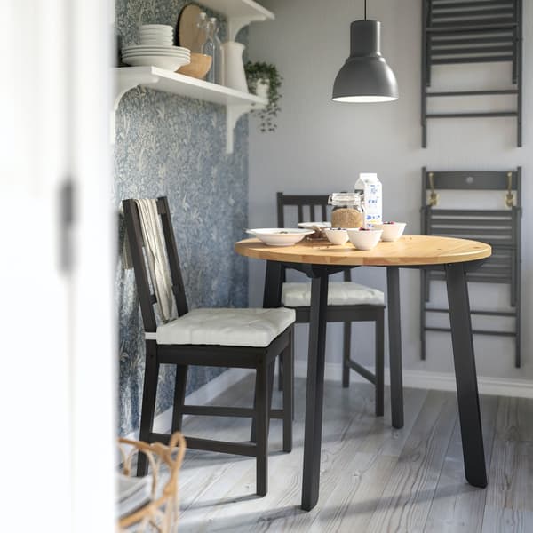 Breakfast set on a round GAMLARED table, two black STEFAN chairs, a grey pendant above and folded chairs on the wall.