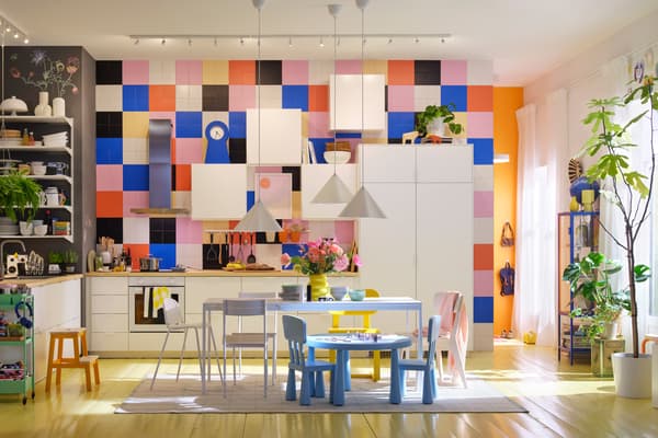 Bright and colorful kitchen with white furniture, multicolored tiled wall, central table and children's chairs, in a family and creative space.