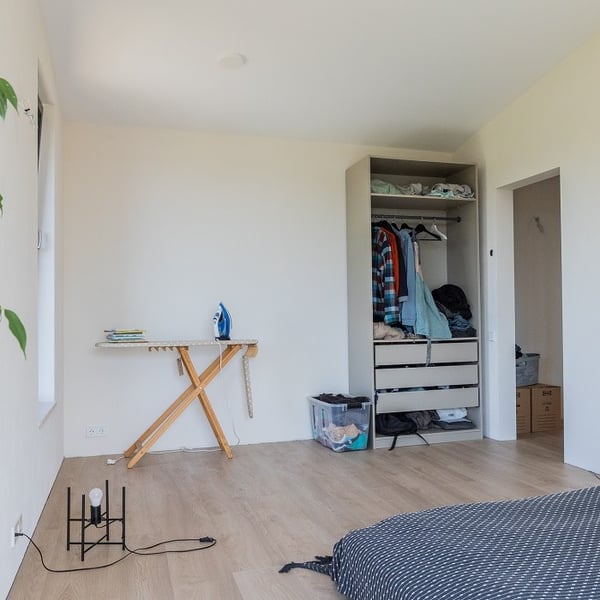 Bright bedroom interior with open wardrobe, ironing board, and minimalist decor