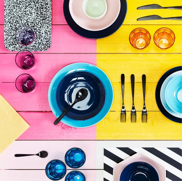 Bright, block-colored surface with a variety of colored bowls, cutlery and glasses laid out across it.