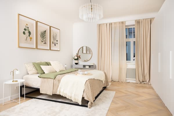 Bright, cosy bedroom with a double bed, neutral textiles, wall art, a round mirror and a wooden parquet floor.