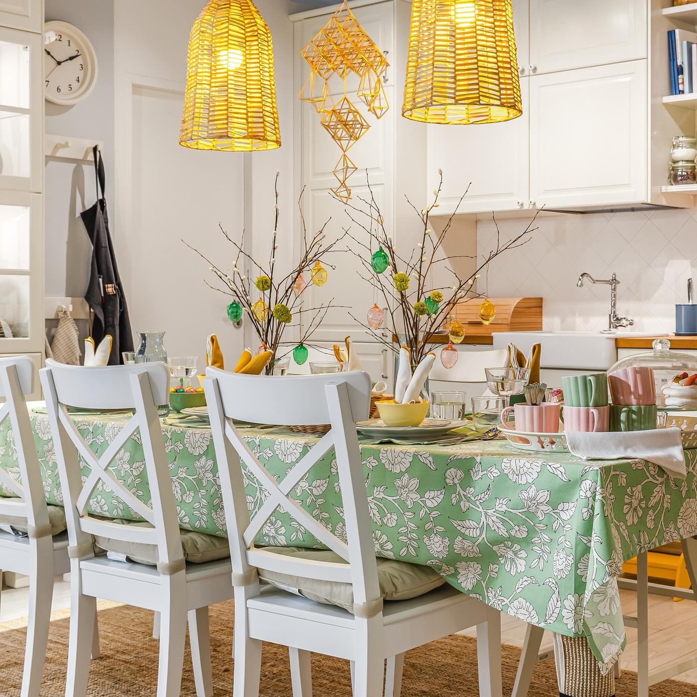 Bright dining area with a green patterned tablecloth, spring decorations and rattan pendant lights creating a cheerful Easter atmosphere.