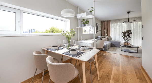 Bright dining area with wooden table, soft chairs, and open-plan living room.