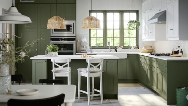 Bright kitchen with green cabinets and white counter tops. Bar with similar coloring and two white counter stools. 