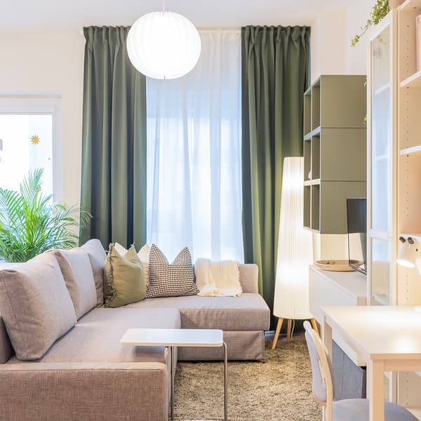 Bright living room with sofa, green curtains, and home office corner.