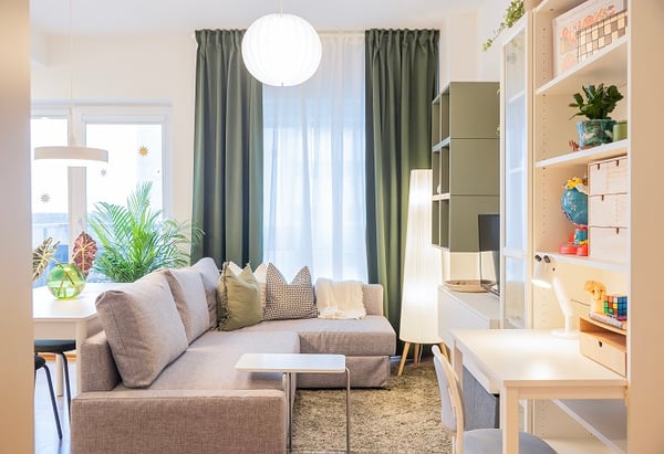 Bright living room with sofa, green curtains, and home office corner.