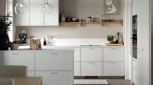 Bright, modern kitchen with white cabinets, a central island, and open wooden shelves displaying bowls and glassware, with pendant lights and small appliances on the countertop.