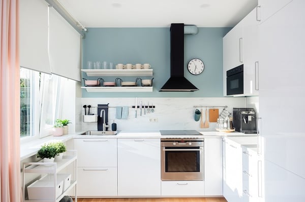 Bright modern kitchen with white cabinets, built-in oven and pastel blue accent wall
