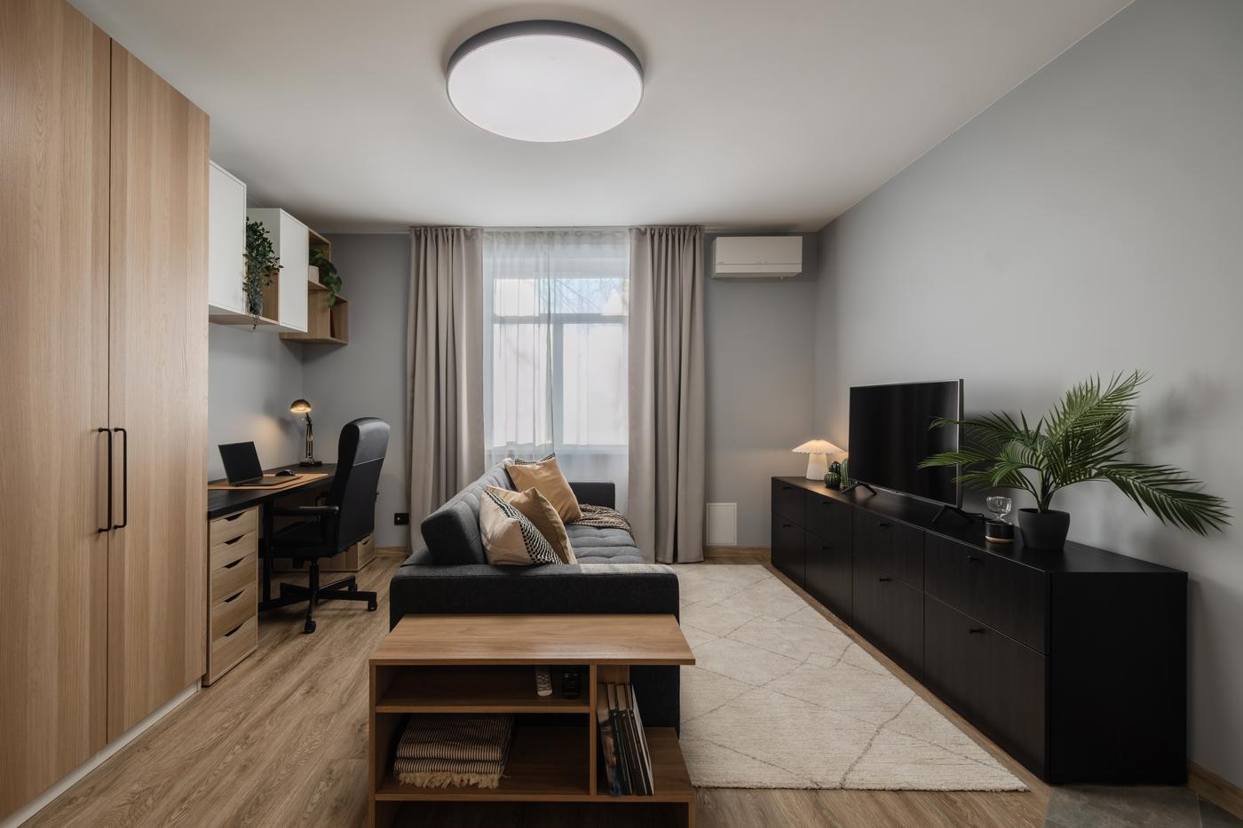 Bright, modern living room with a gray sofa, wooden coffee table, black TV bench, and large window letting in natural light.