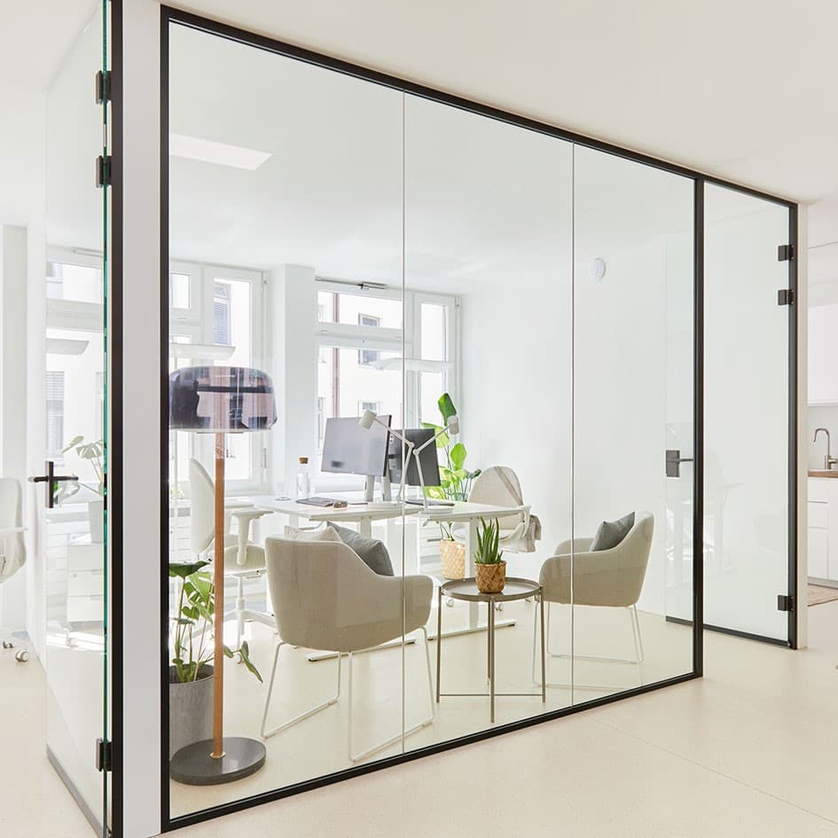 Bright office space behind a glass wall with white desks, light grey office chairs and comfortable armchairs