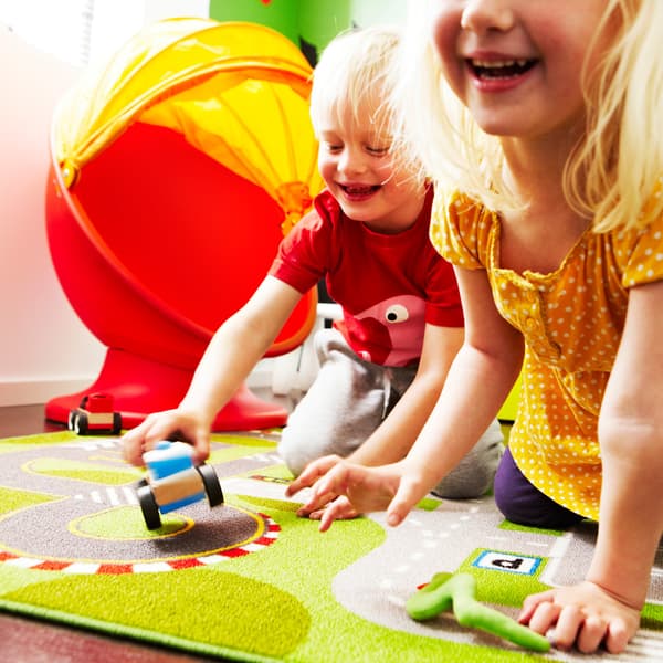 Bright photograph of two children playing on a green carpet. 