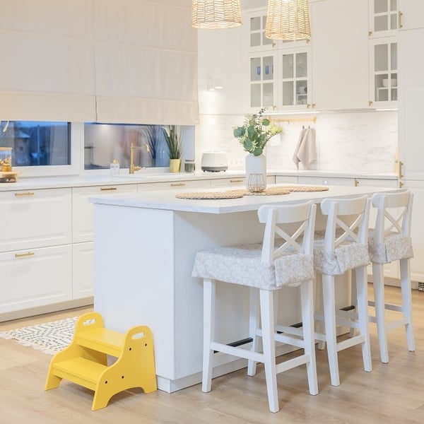 Bright white kitchen with island, bar stools, and yellow step stool for kids.