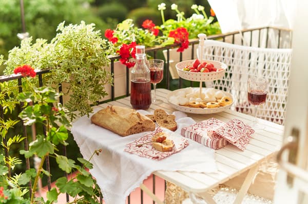 Bröd och saft är uppdukat på ett vitt träbord bredvid svart räcke klätt med blommor