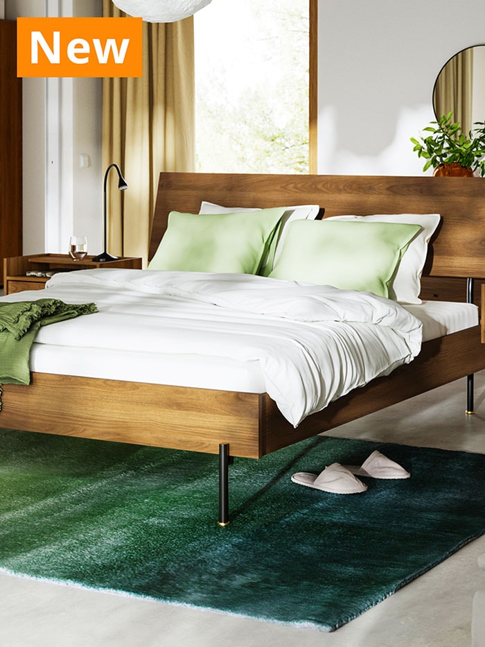 Brown walnut effect RÅDMANSÖ bed frame placed over HOTELLRUM rug in bedroom.