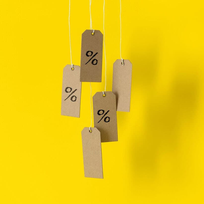 Bruna prisetiketter med %-tecken hänger mot en gul bakgrund.