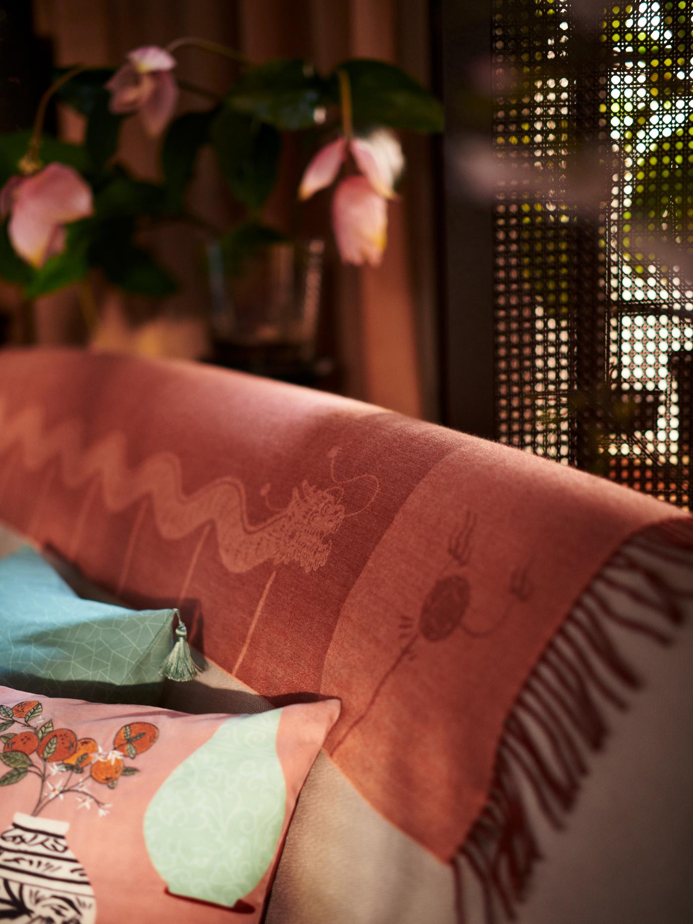 بطانية FÖSSTA بتصميم تنين ملفوفة على ظهر الكنبة التي عليها وسادتان في أغطية وسائد FÖSSTA.