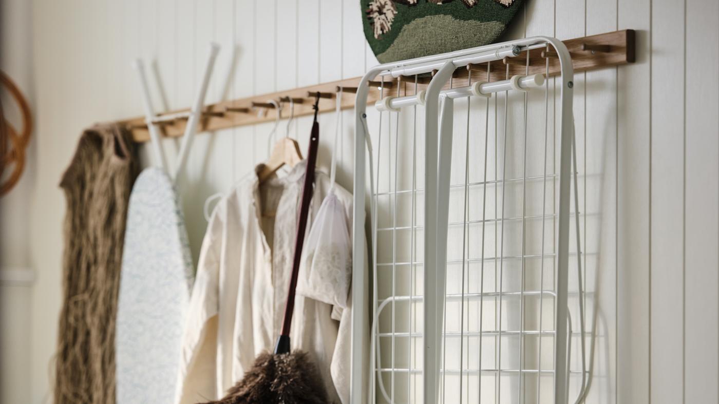 Buanderie, nettoyage et accessoires de repassage suspendus à des portants à 6 boutons HÖVOLM en chêne sur un mur avec lambris blanc.