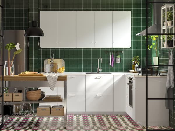 Bucătărie modernă cu mobilier alb, faianță verde închis pe perete și pardoseală cu model colorat. Insulă de bucătărie cu blat din lemn, corpuri de iluminat negre și plante decorative pentru un aer proaspăt și primitor.