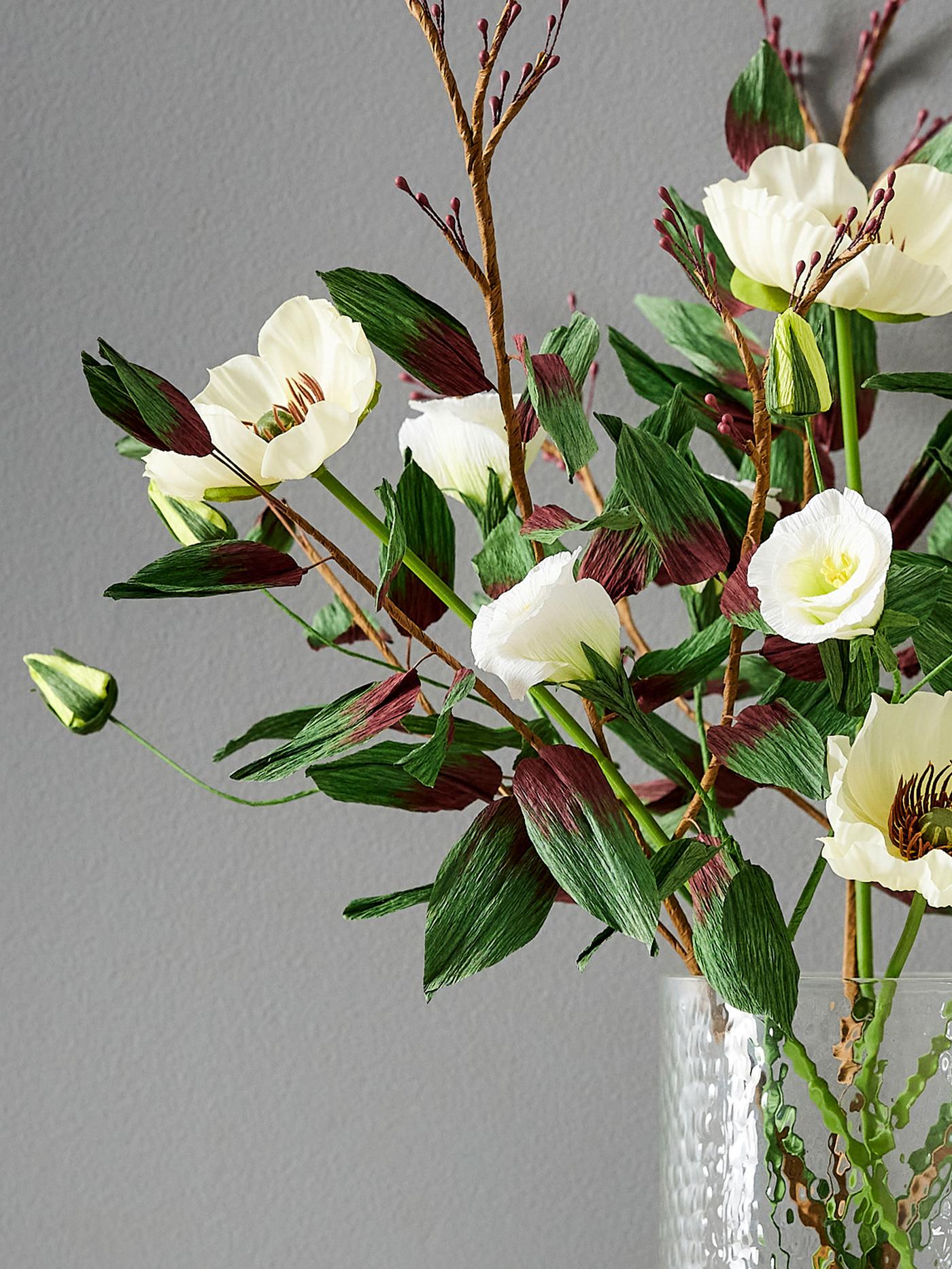 Bukett med naturtrogna konstgjorda snittblommor i ljusa toner arrangerade i vas med gröna kvistar.