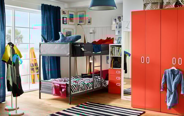 Bunkbeds sit in this bright, colourful children’s room that has a STUVA/FRITIDS wardrobe and bookcase in white/red.